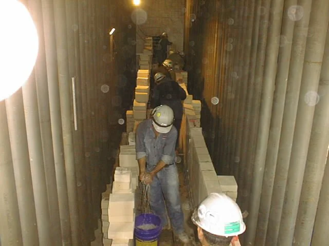 trabajador en pasillo con paredes de ladrillos, colocando ladrillos refractarios  