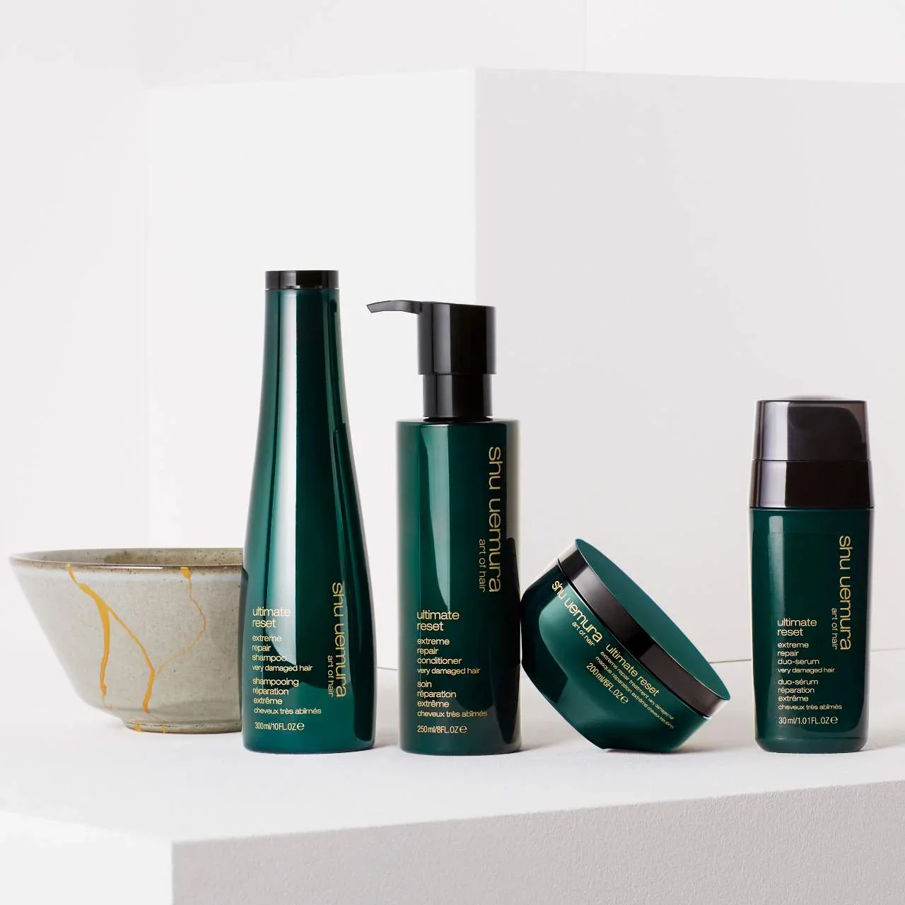 A set of five hair care products from Shu Uemura's Ultimate Reset line, arranged on a white surface with a textured ceramic bowl to the left.