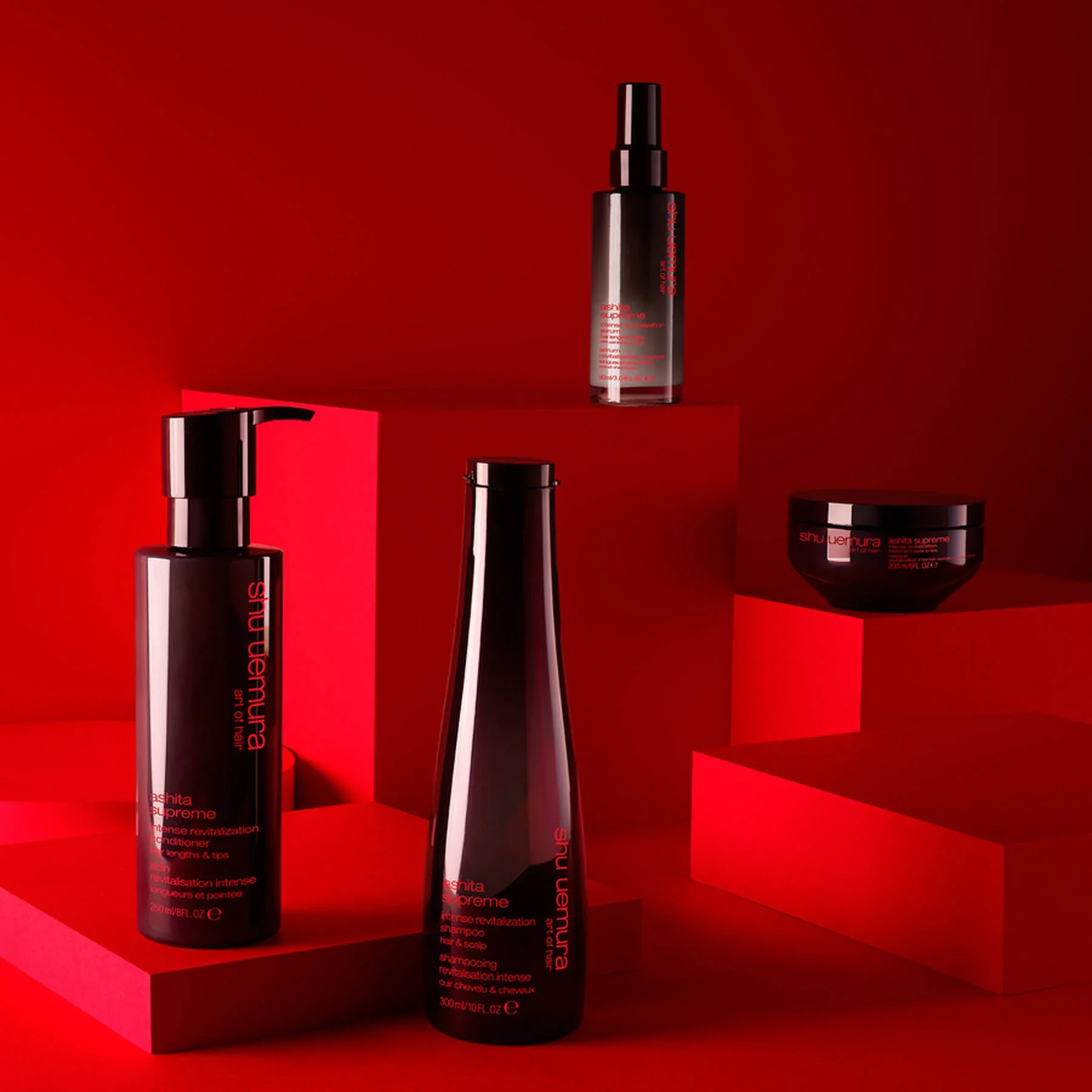 Collection of three Shu Uemura hair care products on red geometric platforms against a red background.