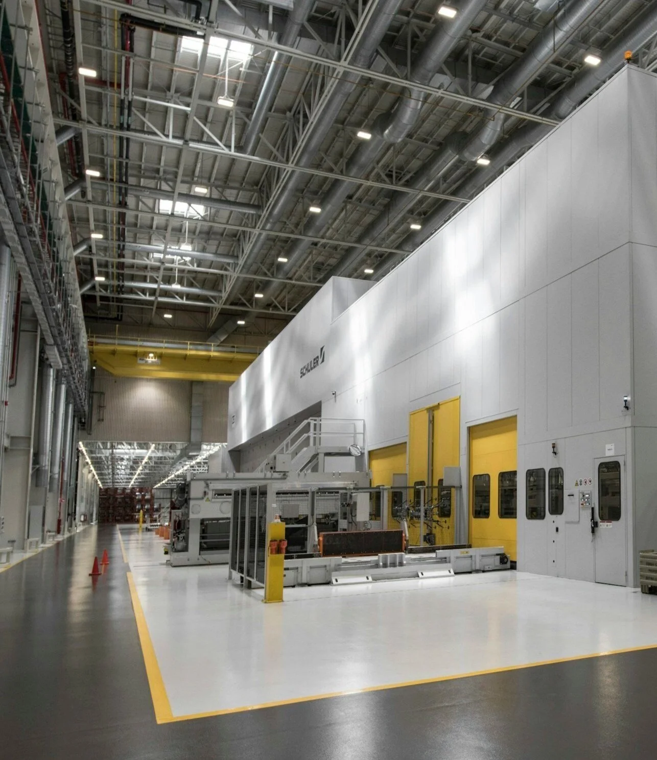 Large industrial manufacturing facility with high ceiling, machinery, and yellow safety doors.