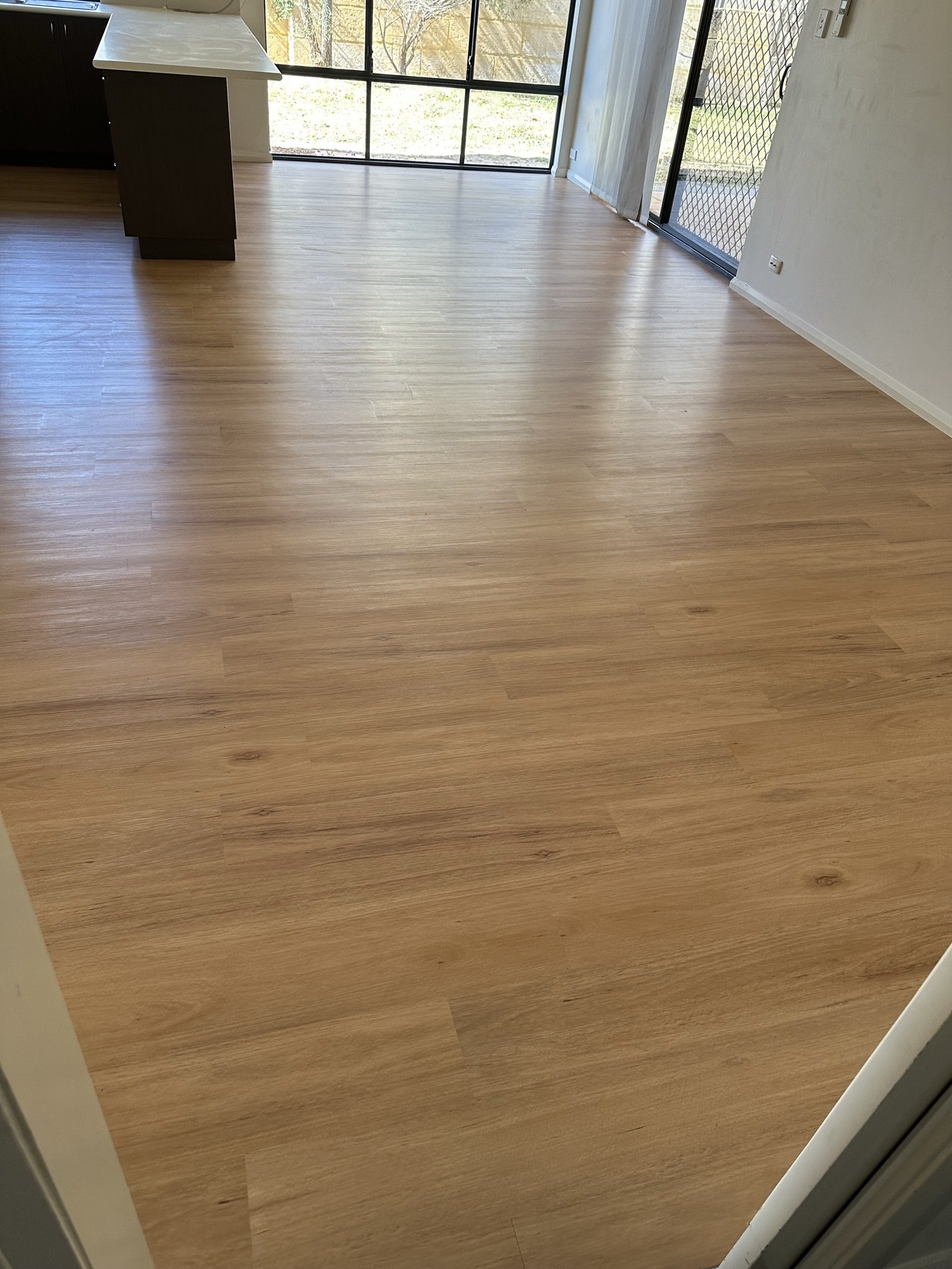 Empty room with light-colored wooden flooring, sliding glass doors, and windows showing an outdoor view.