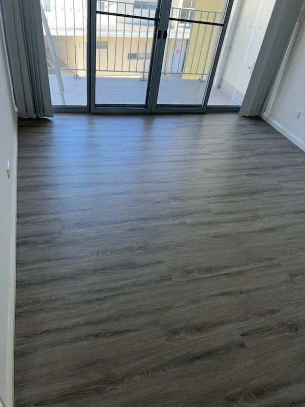 Empty room with wooden flooring and a glass sliding door leading to a small balcony.