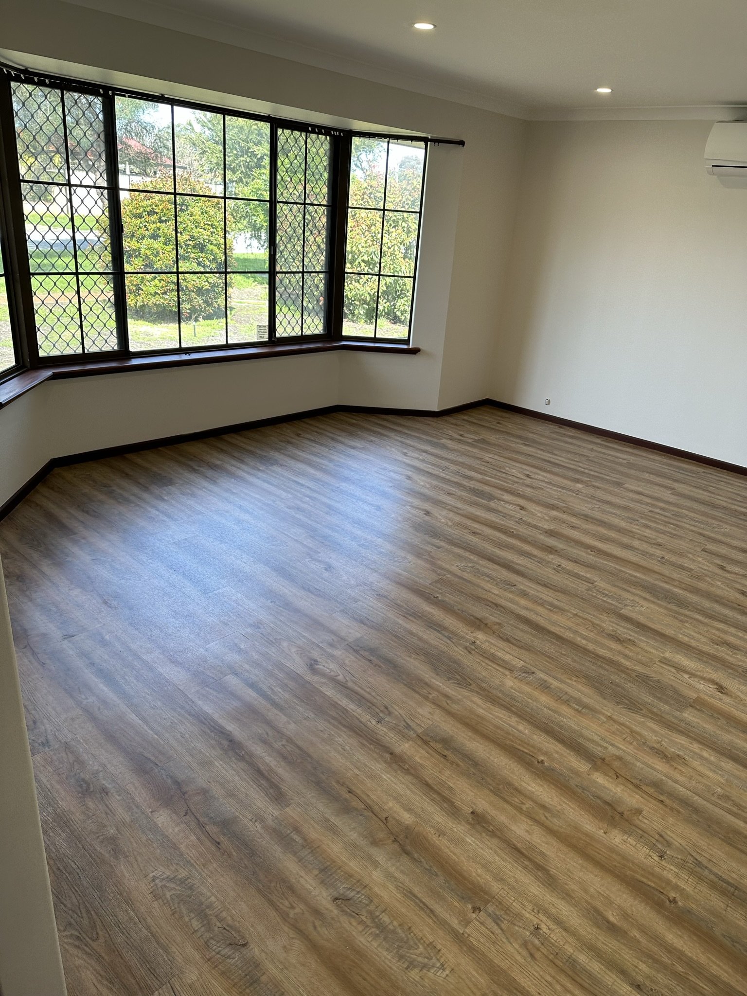 Empty room with large bay window, wood flooring, and a wall-mounted air conditioning unit.