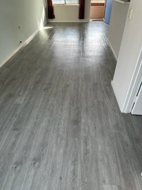 Empty room with gray wooden flooring, pale green walls, and a door leading to a balcony or outdoor area.