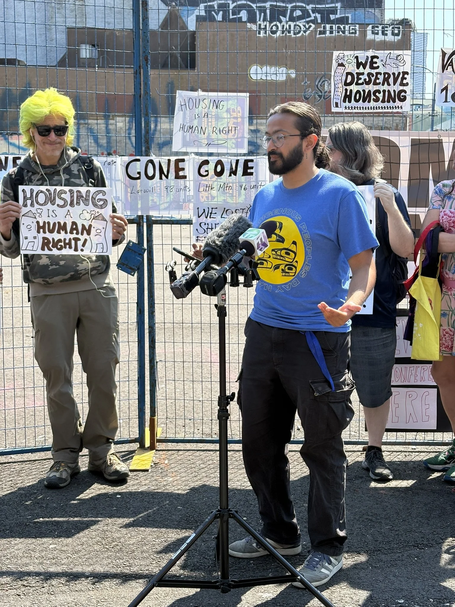 CHP staff Kabir Madan speaks at a July 6, 2026, press conference, with signs and supporters in the background, advocating for housing.