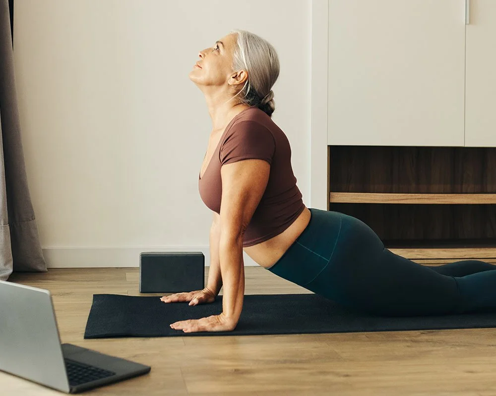 older woman doing yoga in her living room next to an ipad