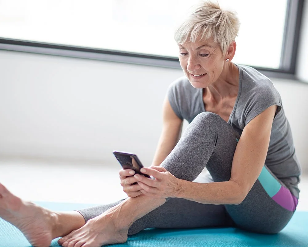 older woman on yoga mat typing on mobile phone