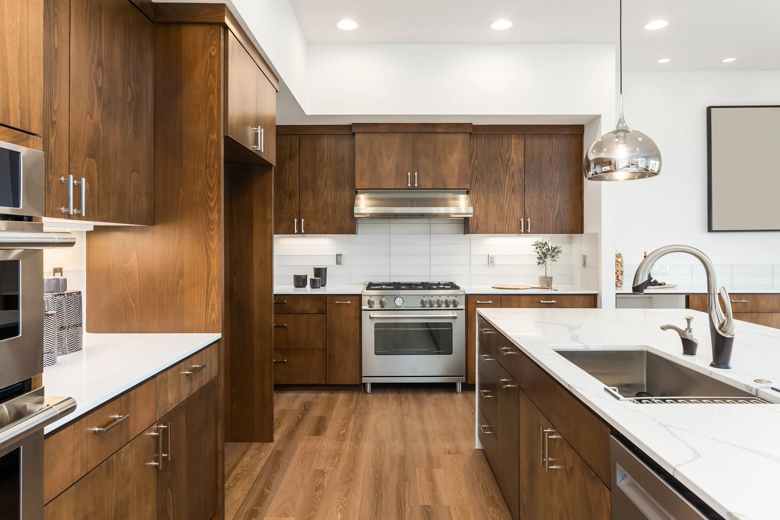 Modern kitchen with wooden cabinets, white countertops, stainless steel appliances, and a large island with a sink and chrome faucet.