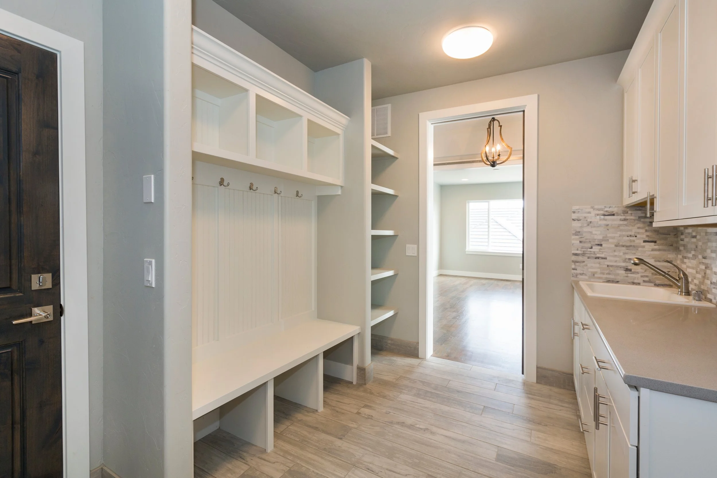 Entryway with white built-in bench and hooks, open shelving, and a view into a room with hardwood floors and a window.