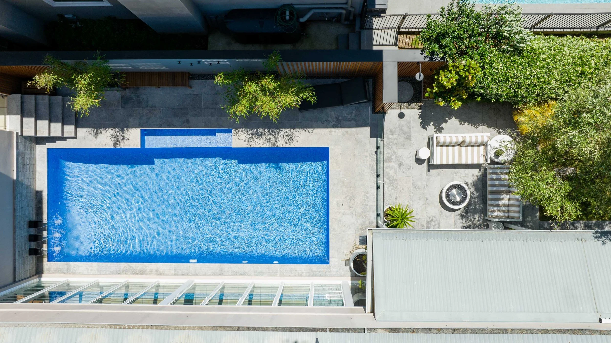 Aerial view of a modern outdoor patio with a swimming pool, lounge chairs, and greenery surrounding the area.