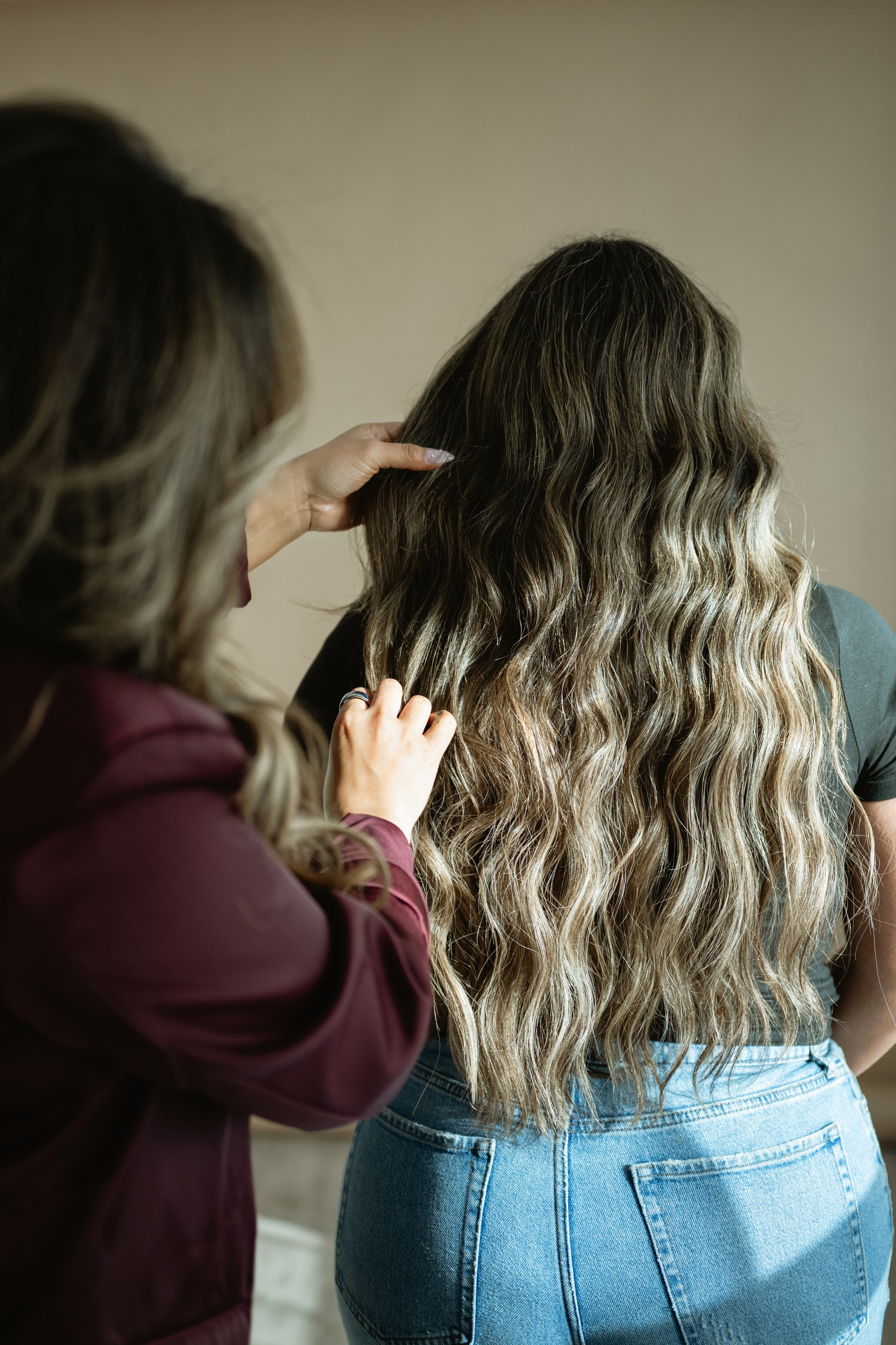 Back view of 2 rows of hair extensions  blonde dimensional hair color, wearing a black top, standing indoors. Natural looking hair extensions.