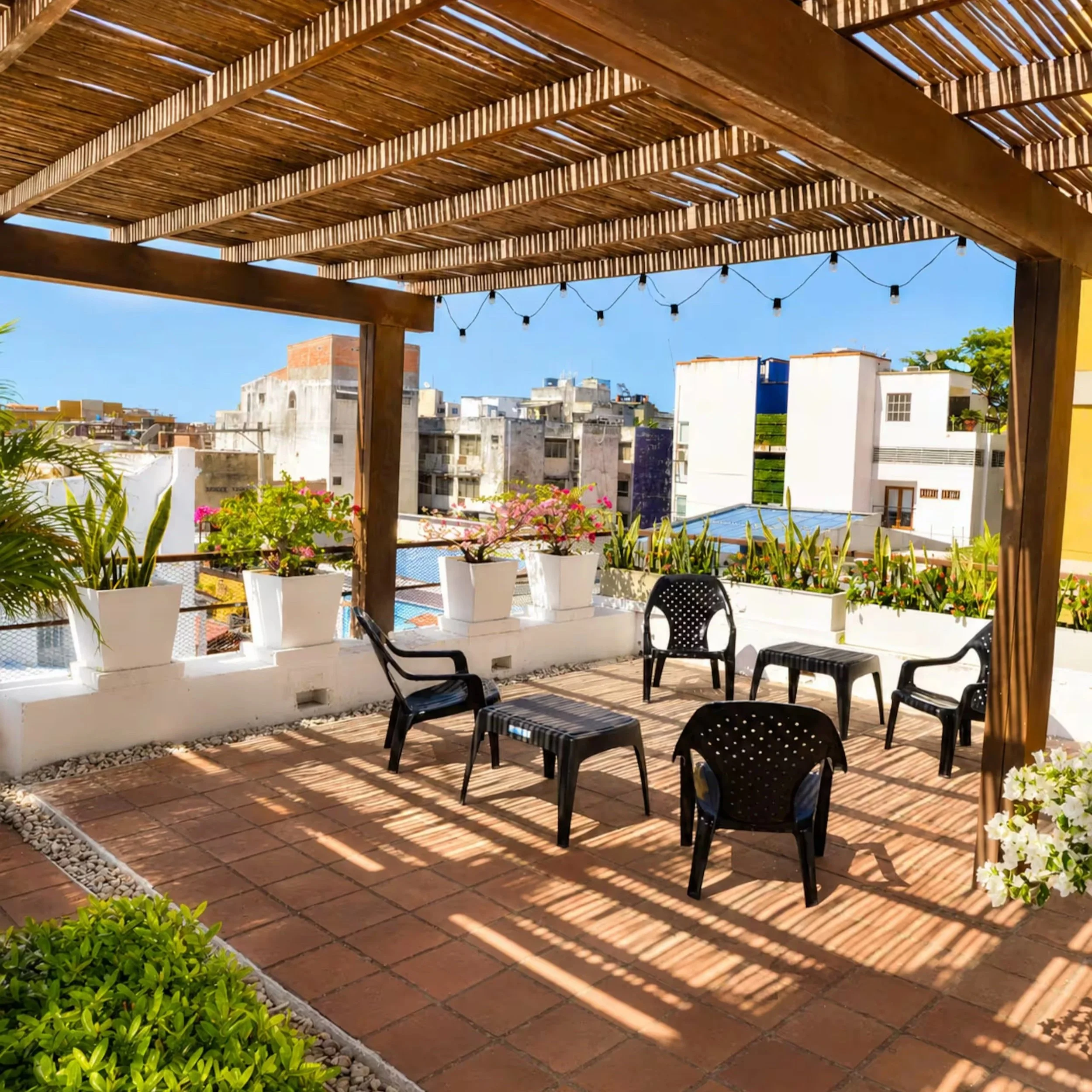 Rooftop terrace with wooden pergola, potted plants, and outdoor furniture in an urban neighborhood.