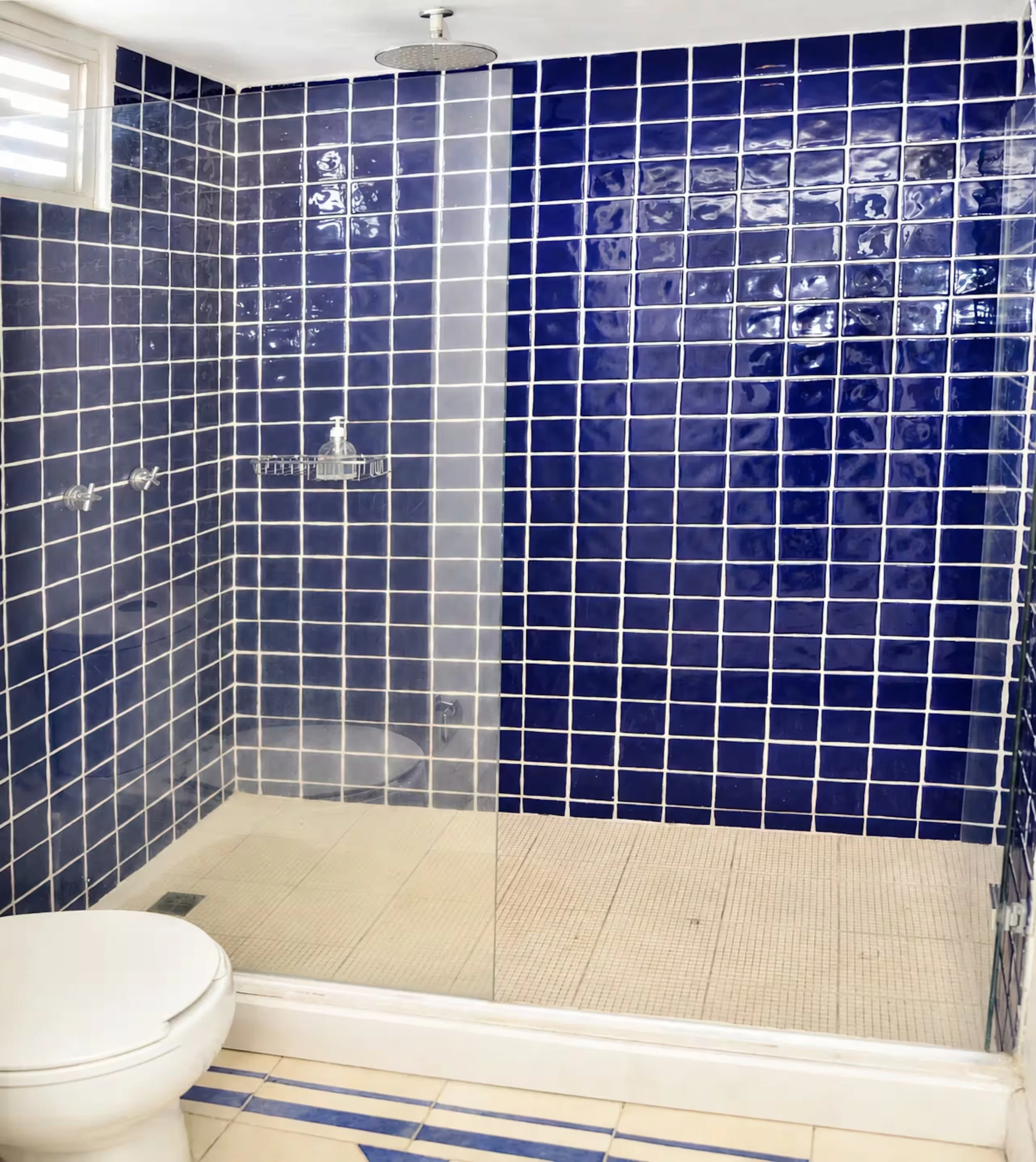 Bathroom shower with blue tiled walls, a silver showerhead, and a white tiled floor with a striped pattern.