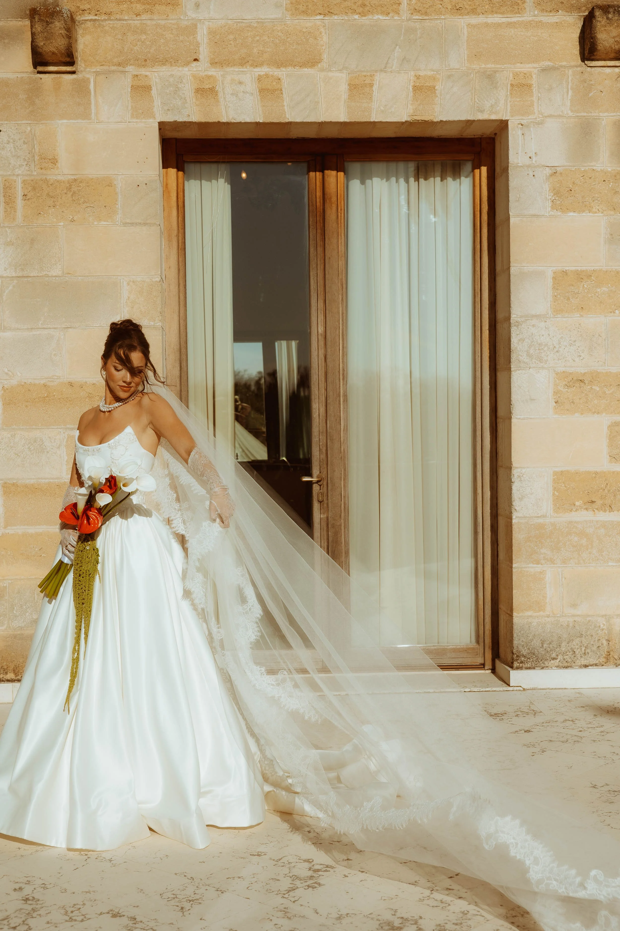 Rosalina poses in a Studio I Do Bridals wedding dress against the soft stone of Masseria Quadrelli