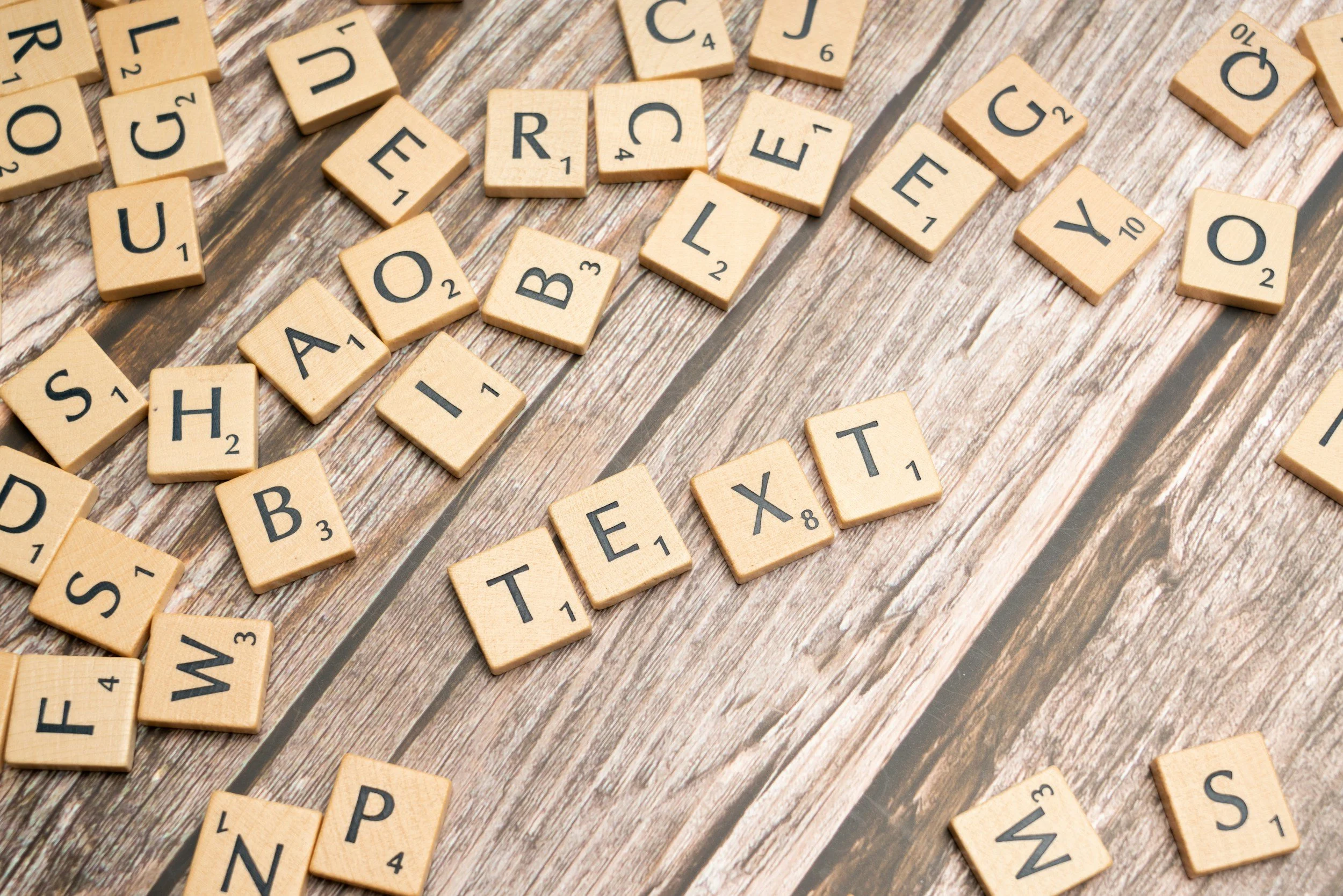 Scrabble tiles spread out on a wooden surface, with some tiles spelling 'TOUR' and 'E', among other letter tiles.
