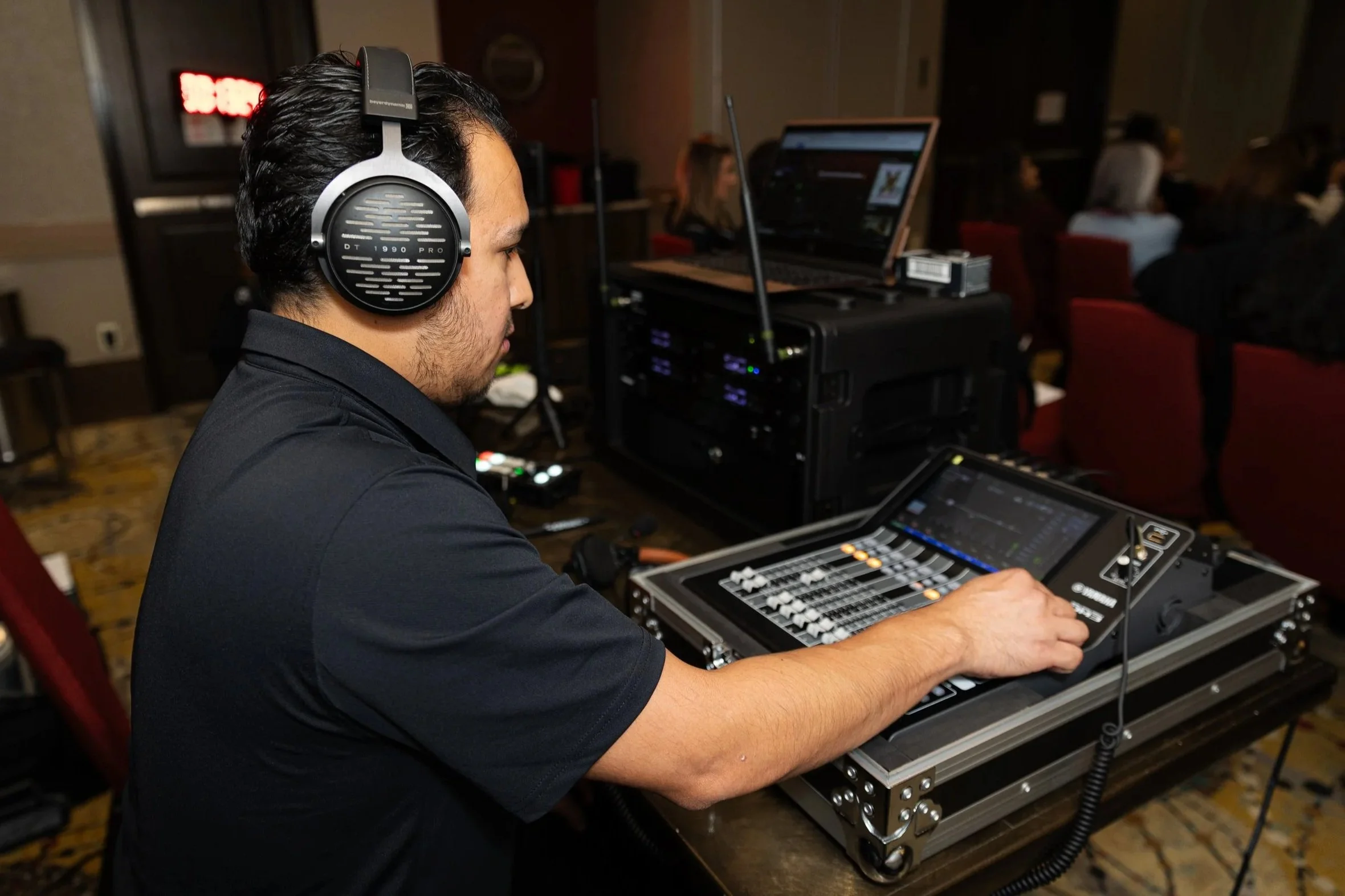 A person working at a music mixing console with illuminated digital screens and colorful illuminated controls in a dark environment.