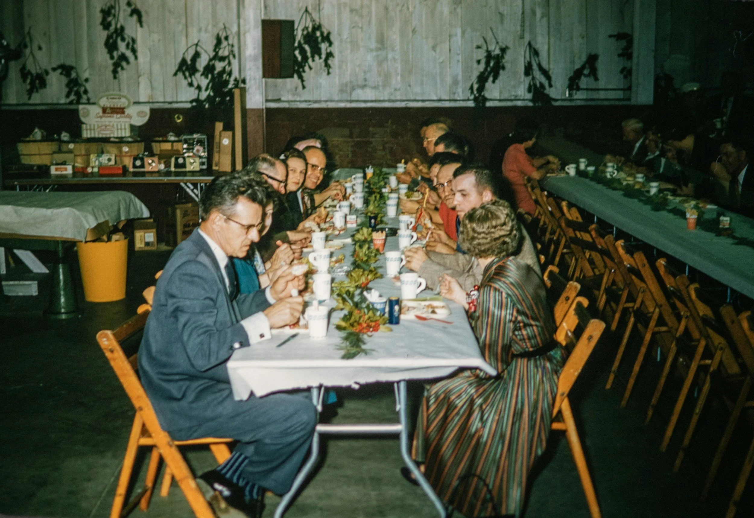 People sitting at a long Christmas dinner table, eating and drinking, with holiday decorations on the table and a decorated room in the background.