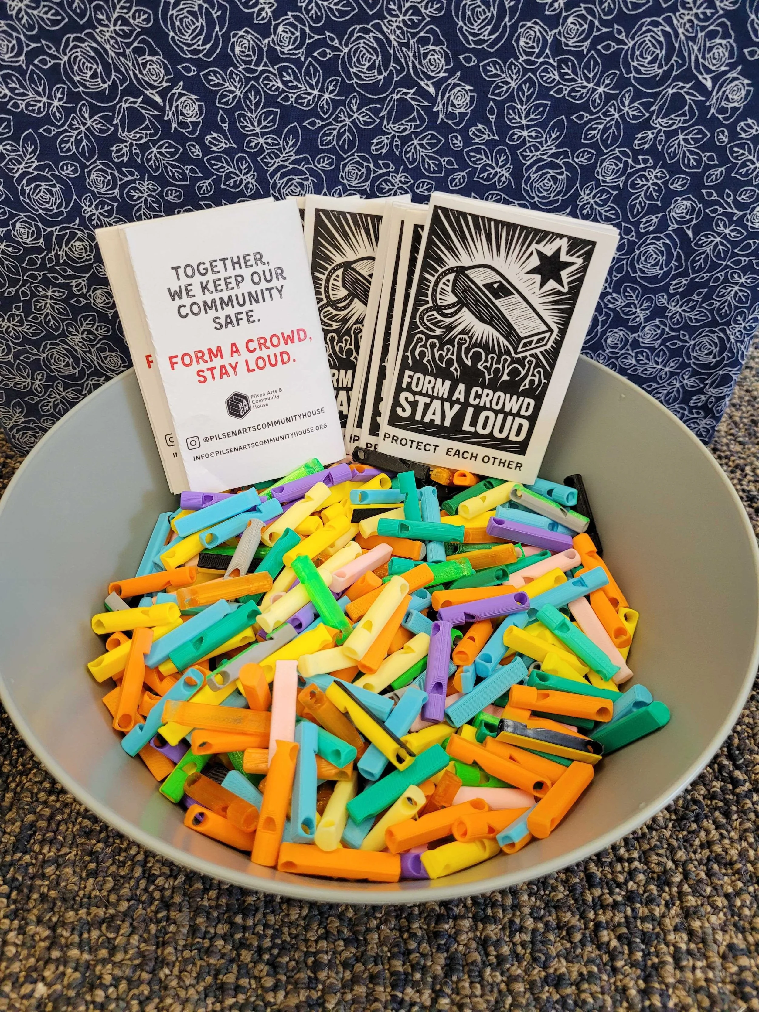 A light grey bowl containing black, white, and red zines, and many brightly colored, 3D printed whistles.