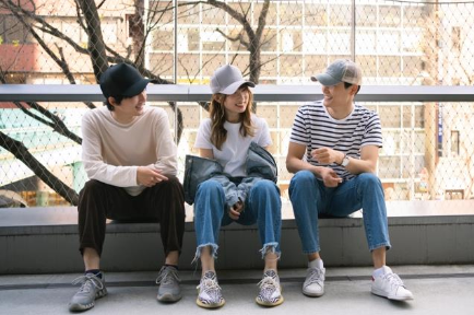 Three youth sit on a curb or low wall with a fence behind them.