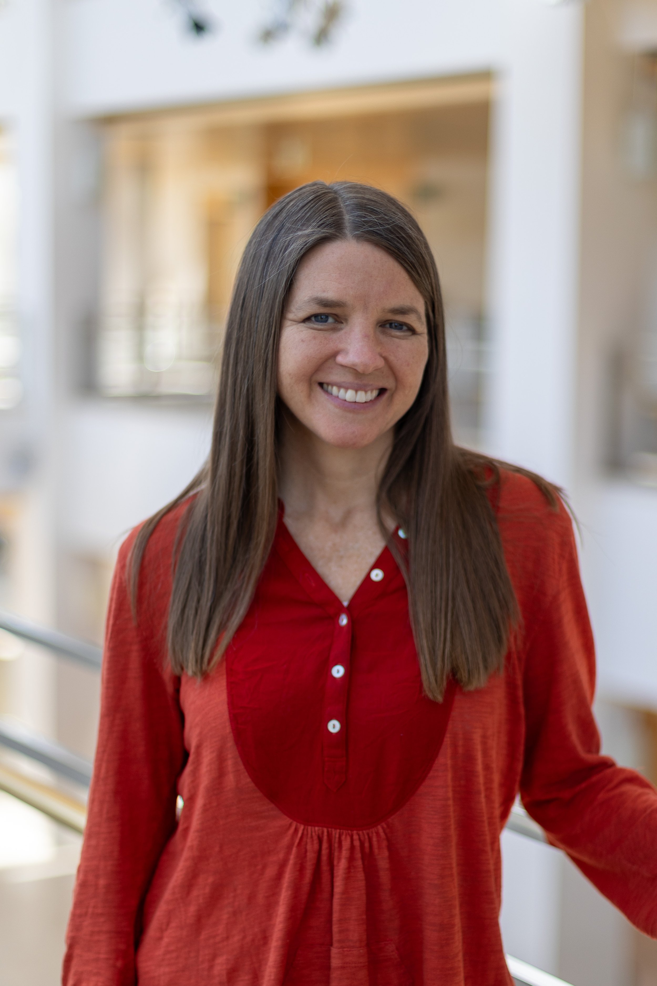 A white woman wtih long, brown hair, wearing red.