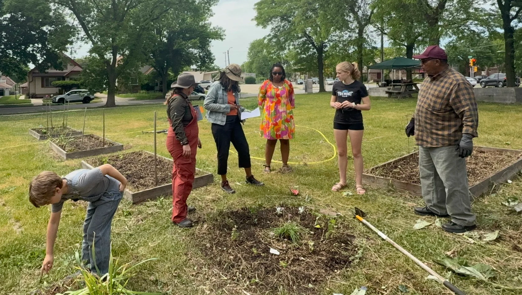 A group of people stand between slightly raised garden beds, discussing plans for sowing companion plants. Location: St Mark AME Community Garden, Milwaukee.