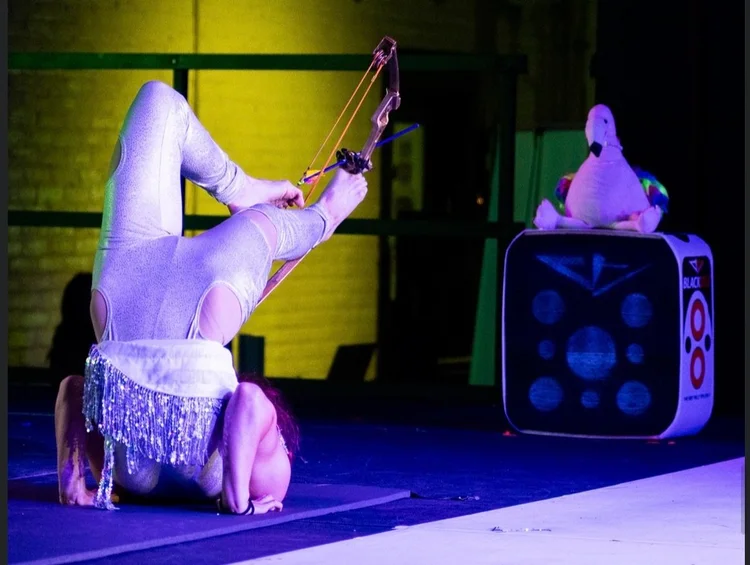 Talia Hazard drawing a bow with her feet under purple stage lighting