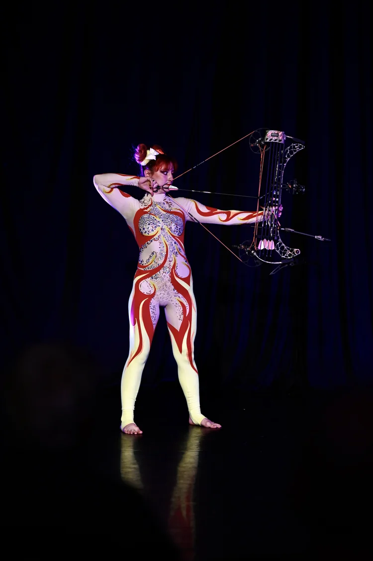 Talia Hazard aiming a compound bow on stage at NECCA