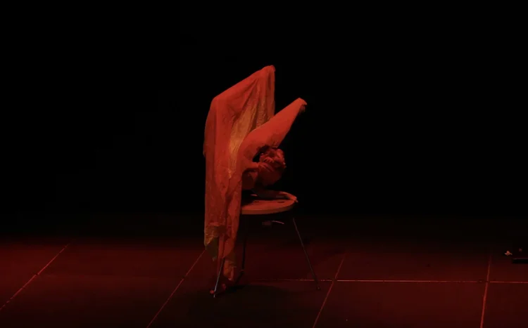 Talia Hazard holding an inverted contortion pose under red stage lighting