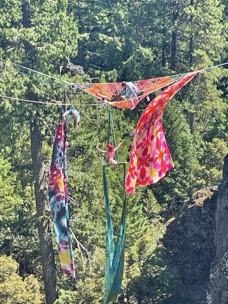 Talia Hazard suspended in colorful aerial silks above a wooded landscape