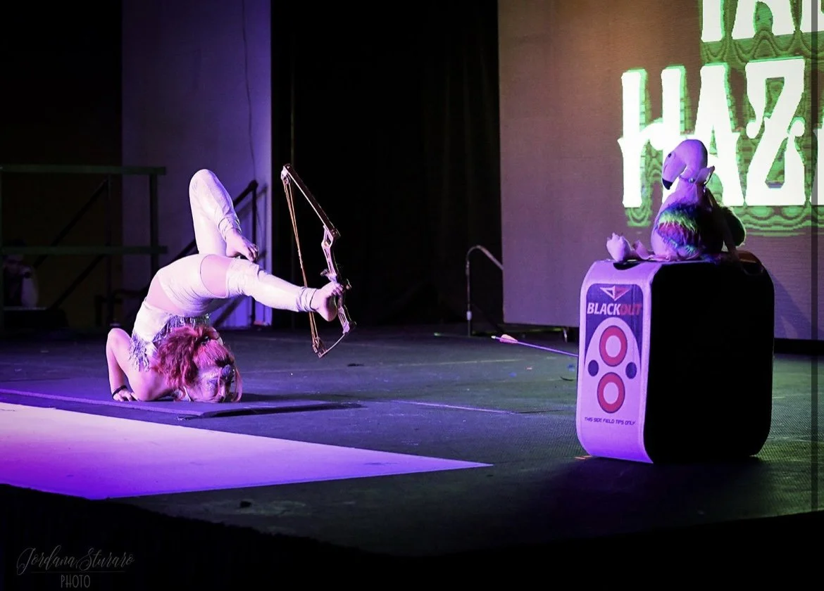 Talia Hazard aiming a foot bow during a purple-lit stage performance