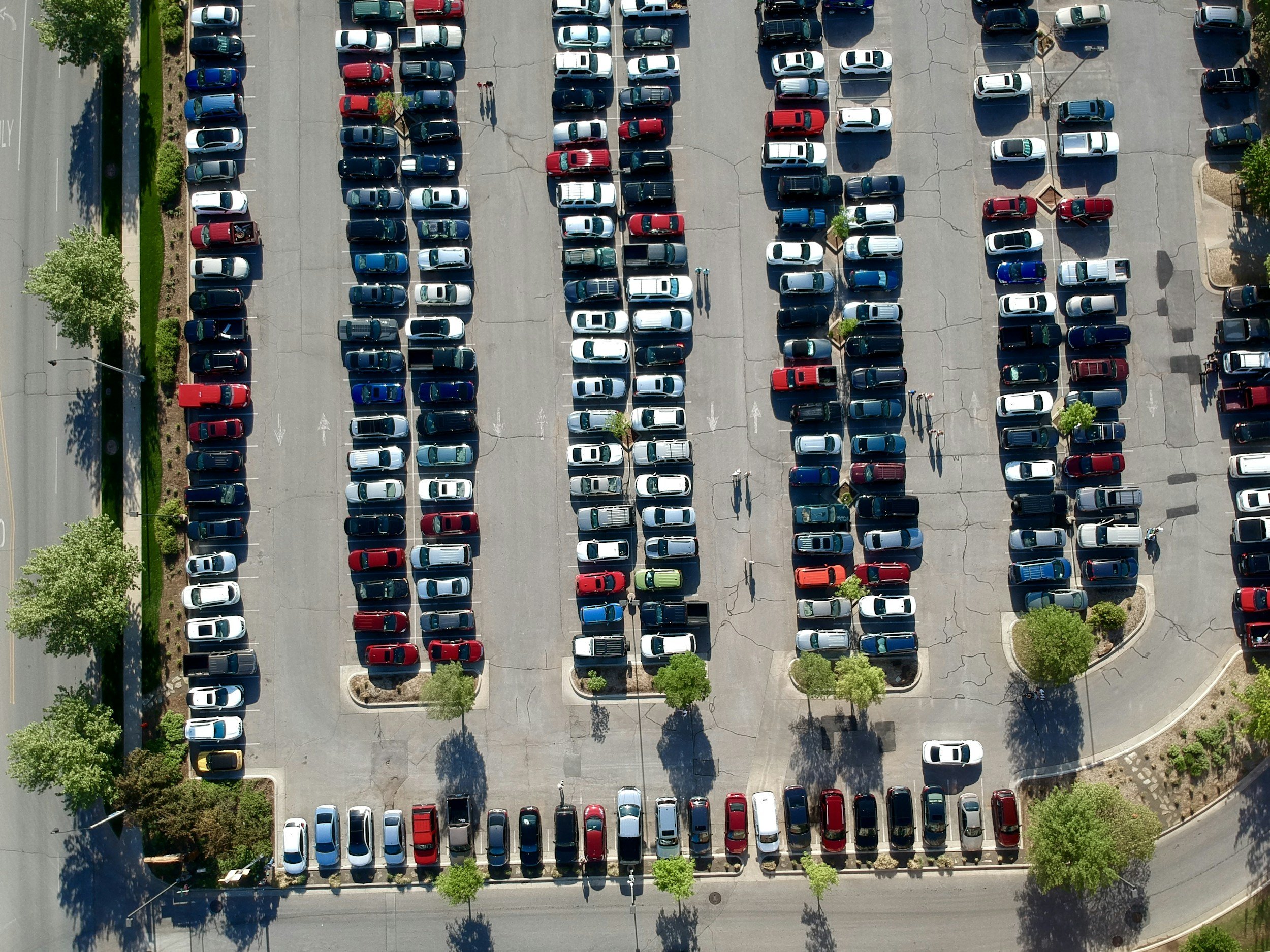 Aerial view of a parking lot filled with cars, with trees along the perimeter and some people walking.