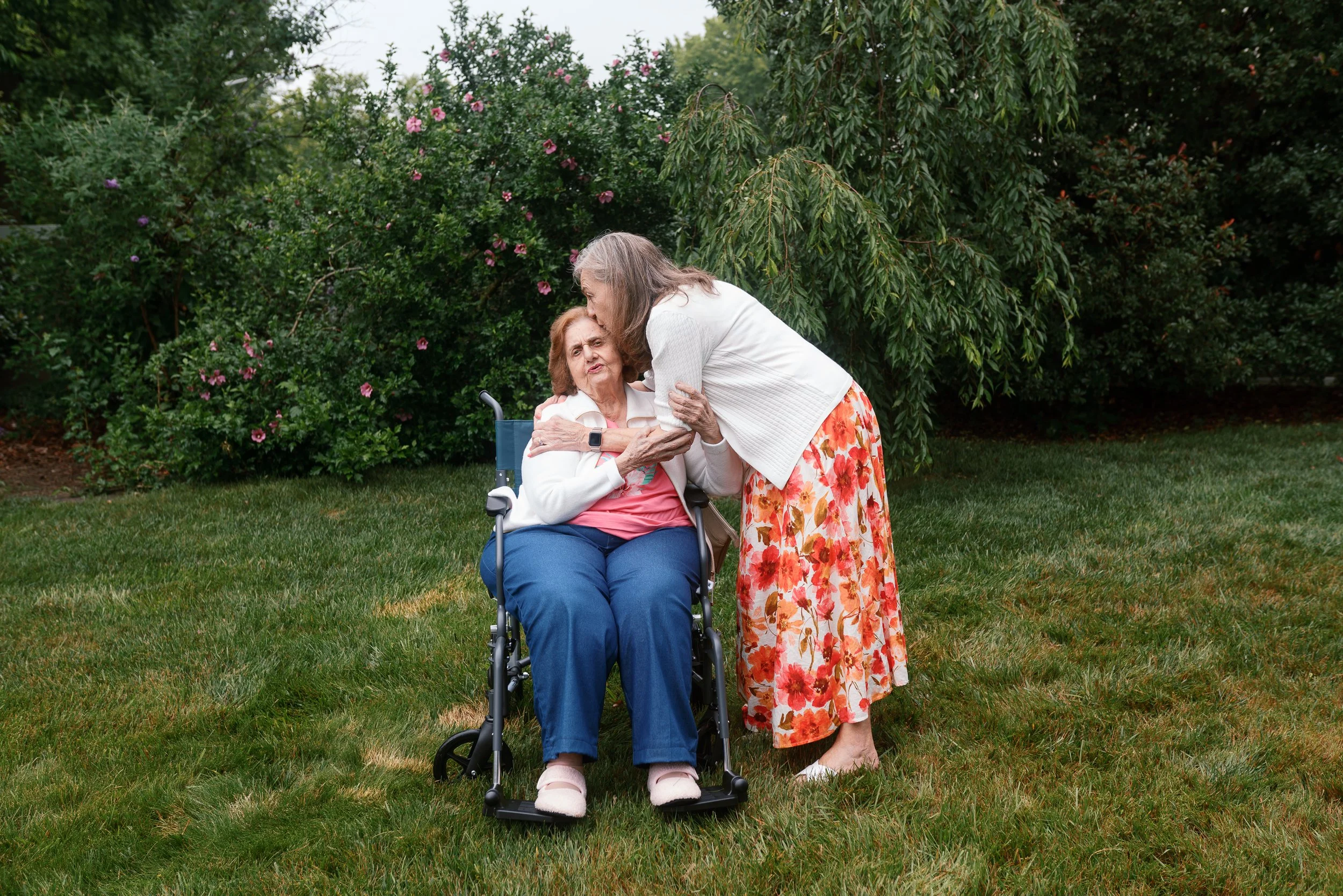 Portrait of a woman kissing her mother's forehead as she sits in her wheelchair at a Haddonfield family reunion.