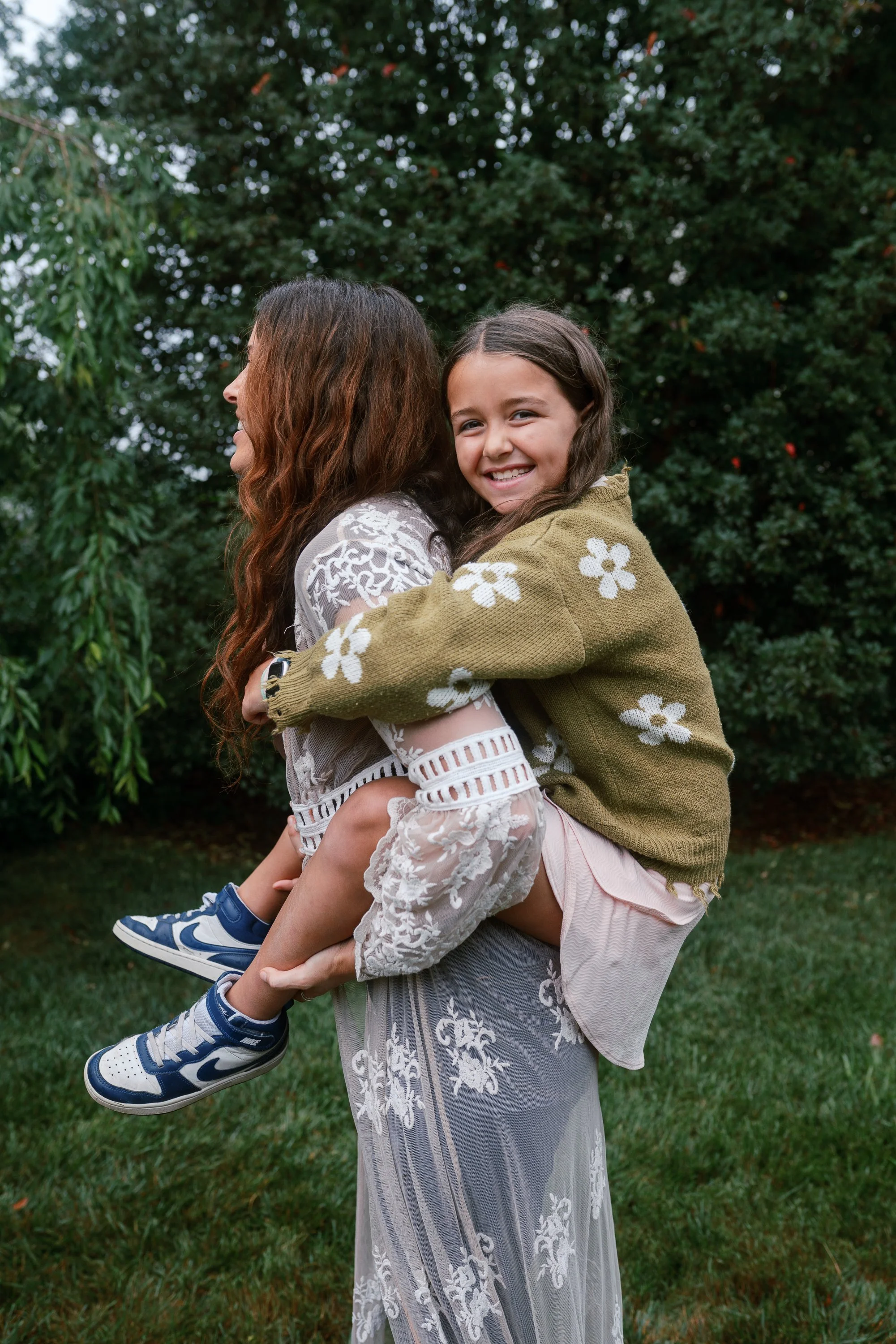 Girl riding piggyback on her mom during a backyard family reunion in Haddonfield, New Jersey