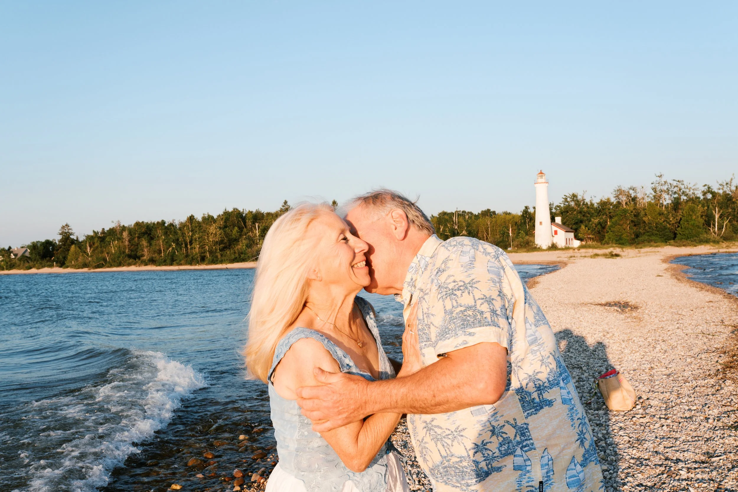 Husband whispering in his wife's ear near the Cape May lighthouse during their anniversary portrait session