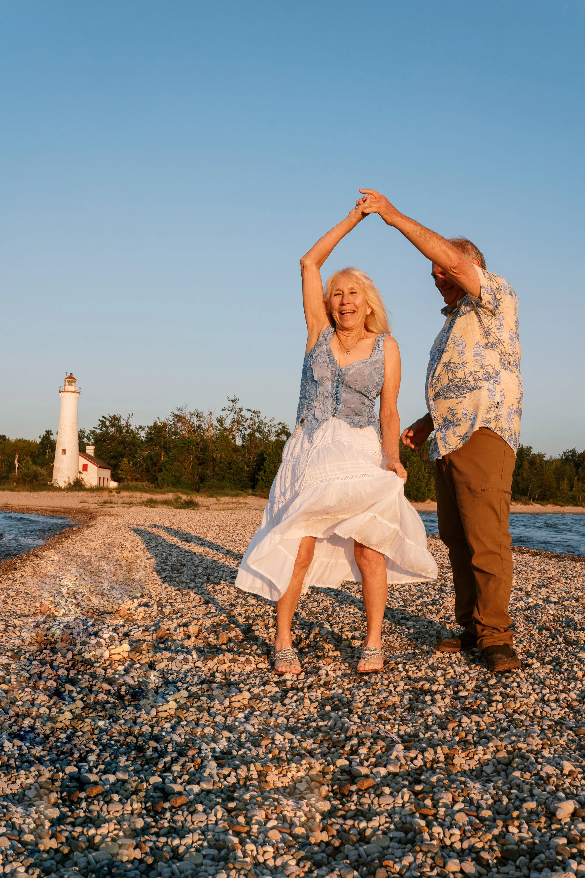 Husband twirling his wife on the beach at Cape May Lighthouse, New Jersey, celebrating fifty years of marriage
