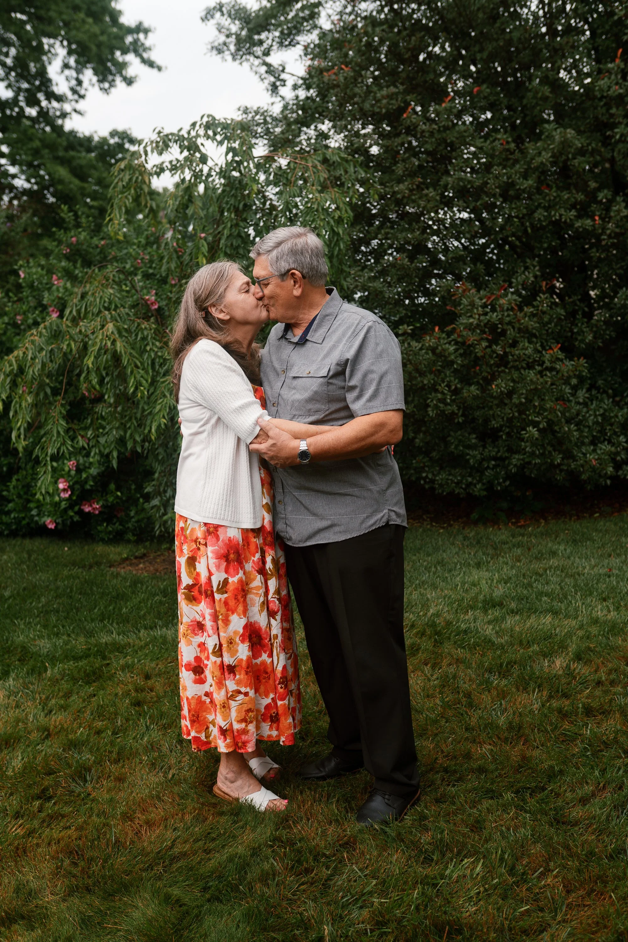 Older couple sharing a kiss in a lush green garden during a South Jersey family reunion portrait session