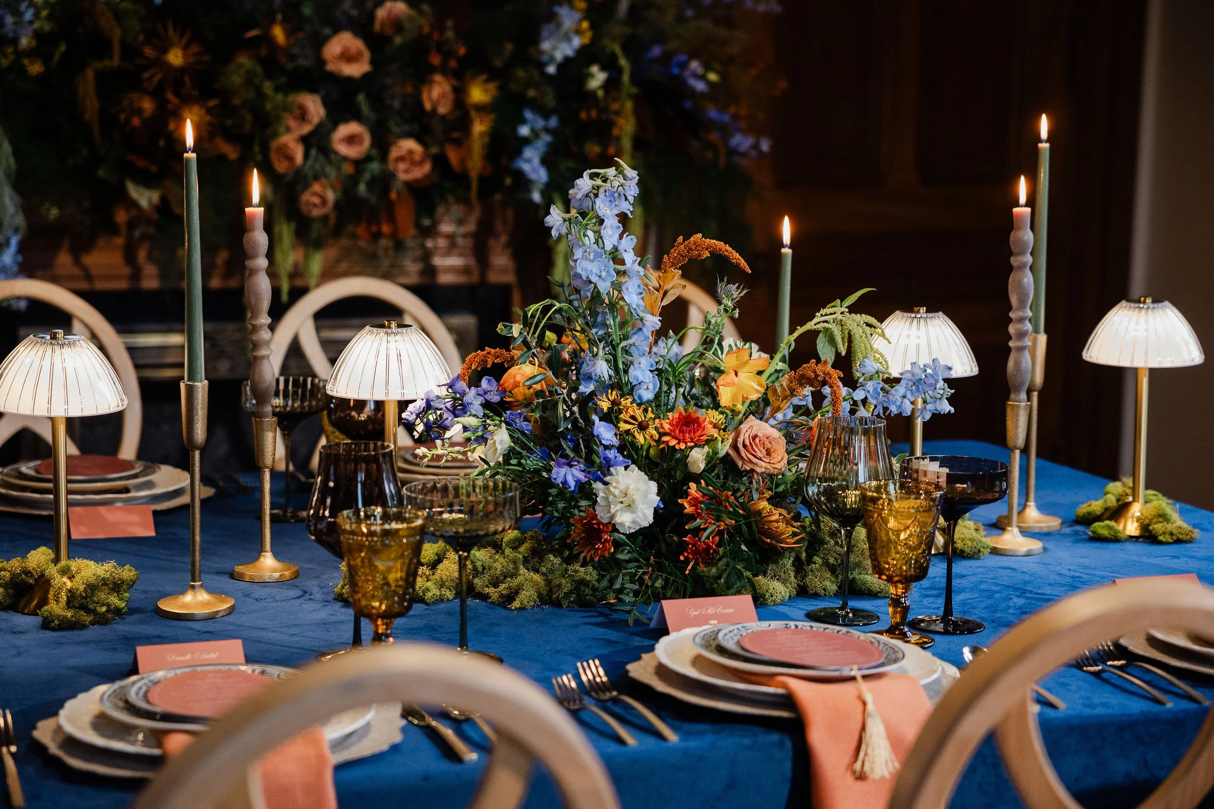A formal dining table set with colorful flowers, candles, and elegant tableware, featuring a lush floral arrangement centerpiece and lit candles for a sophisticated event.