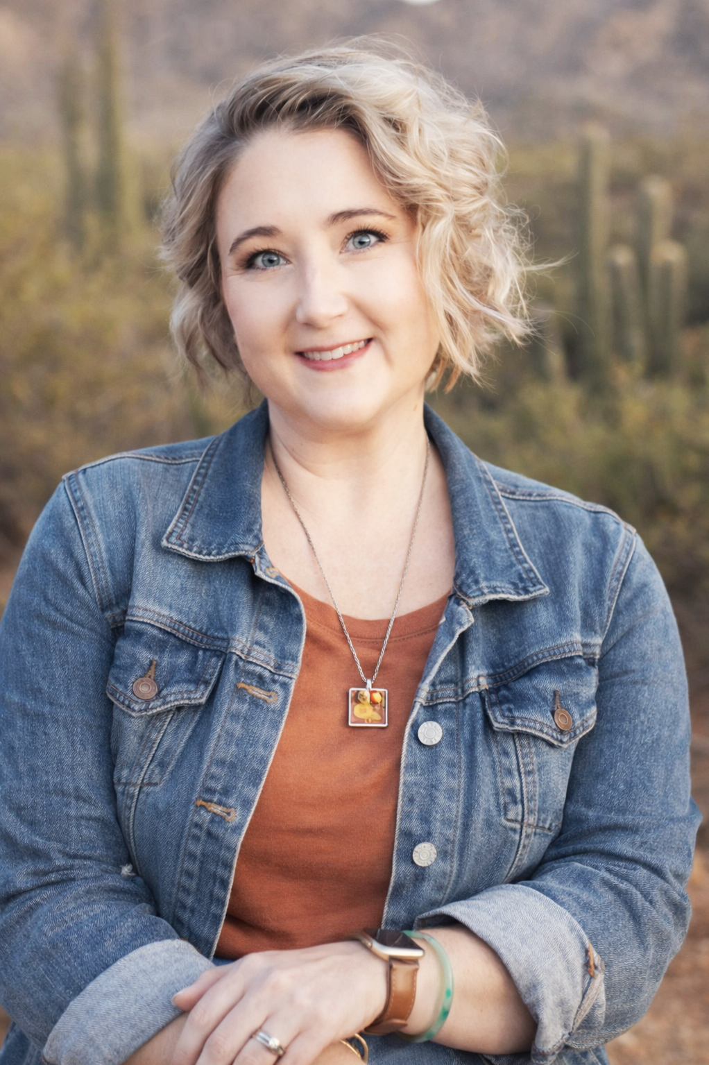 Woman in green patterned dress standing outdoors with desert landscape and cacti in the background.