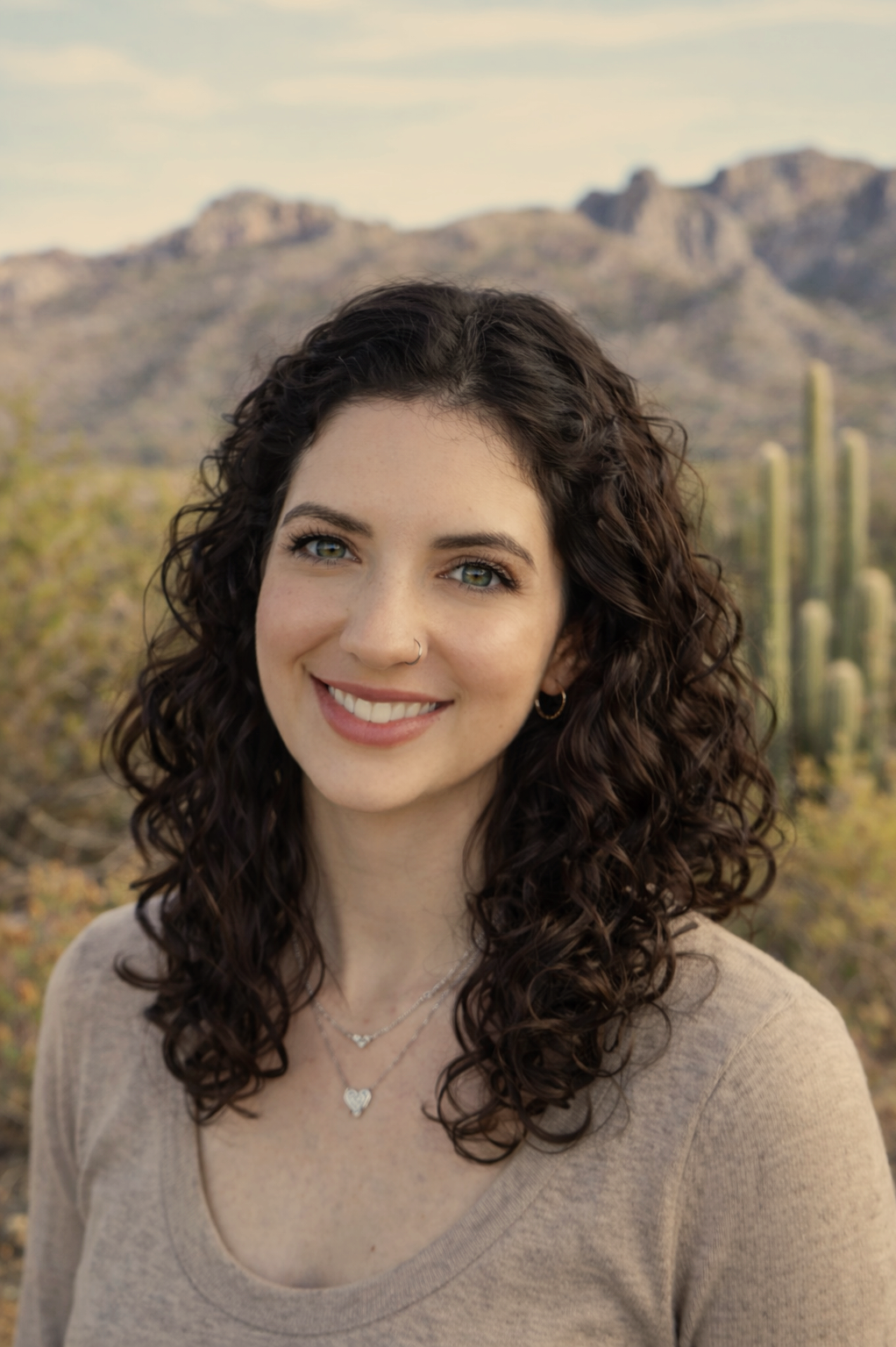 Woman in a green shirt standing in a desert landscape with cacti and mountains in the background.