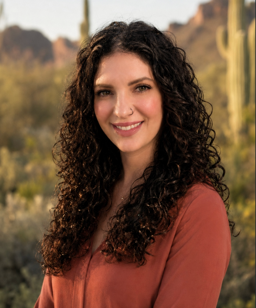 Woman in a green shirt standing in a desert landscape with cacti and mountains in the background.