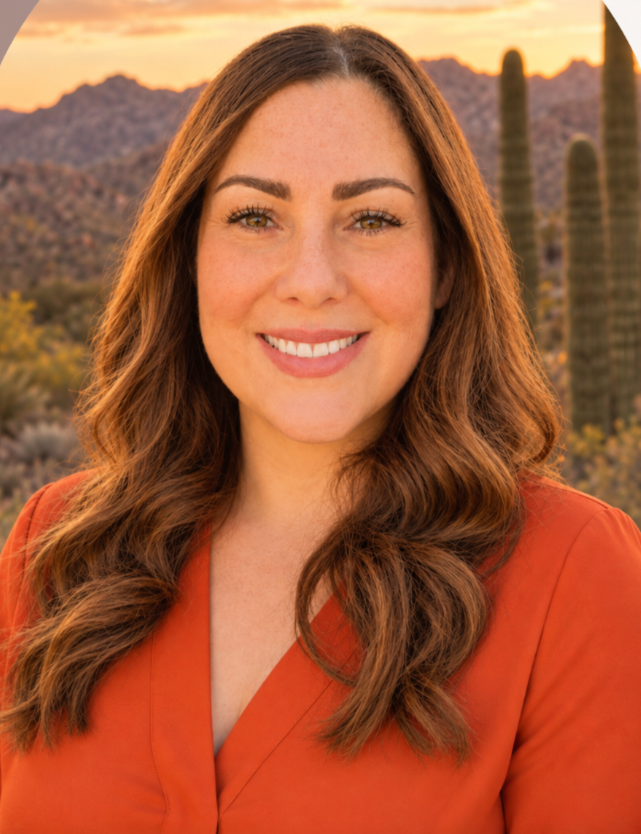 A woman with red hair, wearing large round glasses, smiling with mountains, cacti, and a sunset in the background.