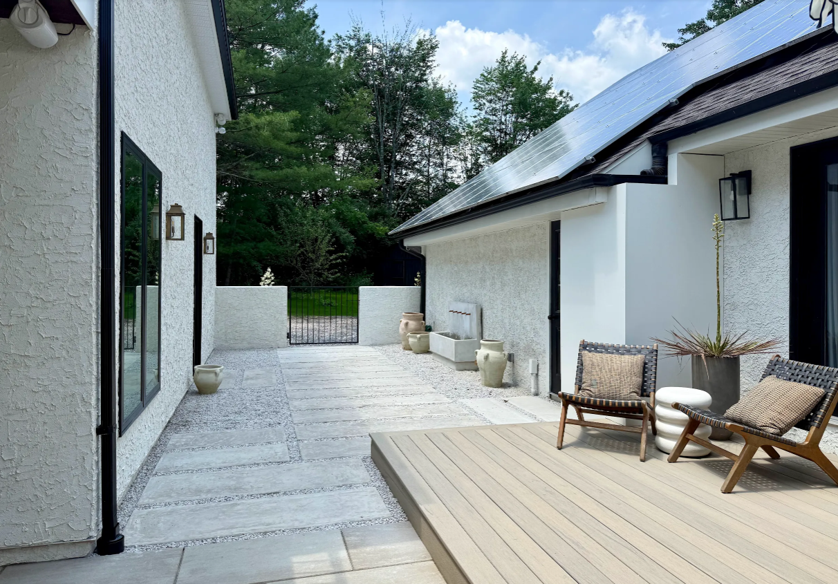 Outdoor patio with seating area, potted plants, and a gate leading to a backyard with trees.