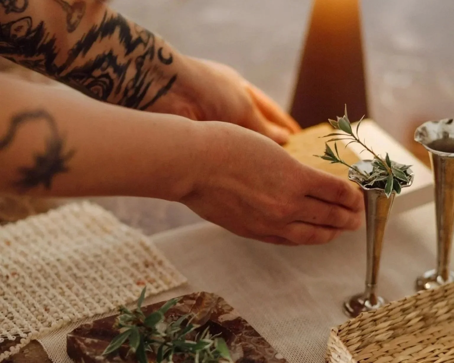 Hände einer Interior Designerin arrangieren Materialmuster auf einem Marmortisch – darunter ein Marmorstein, Natursteinmuster, Leinenstoff und ein Rattantablett, beleuchtet von einer warmen Tischlampe.