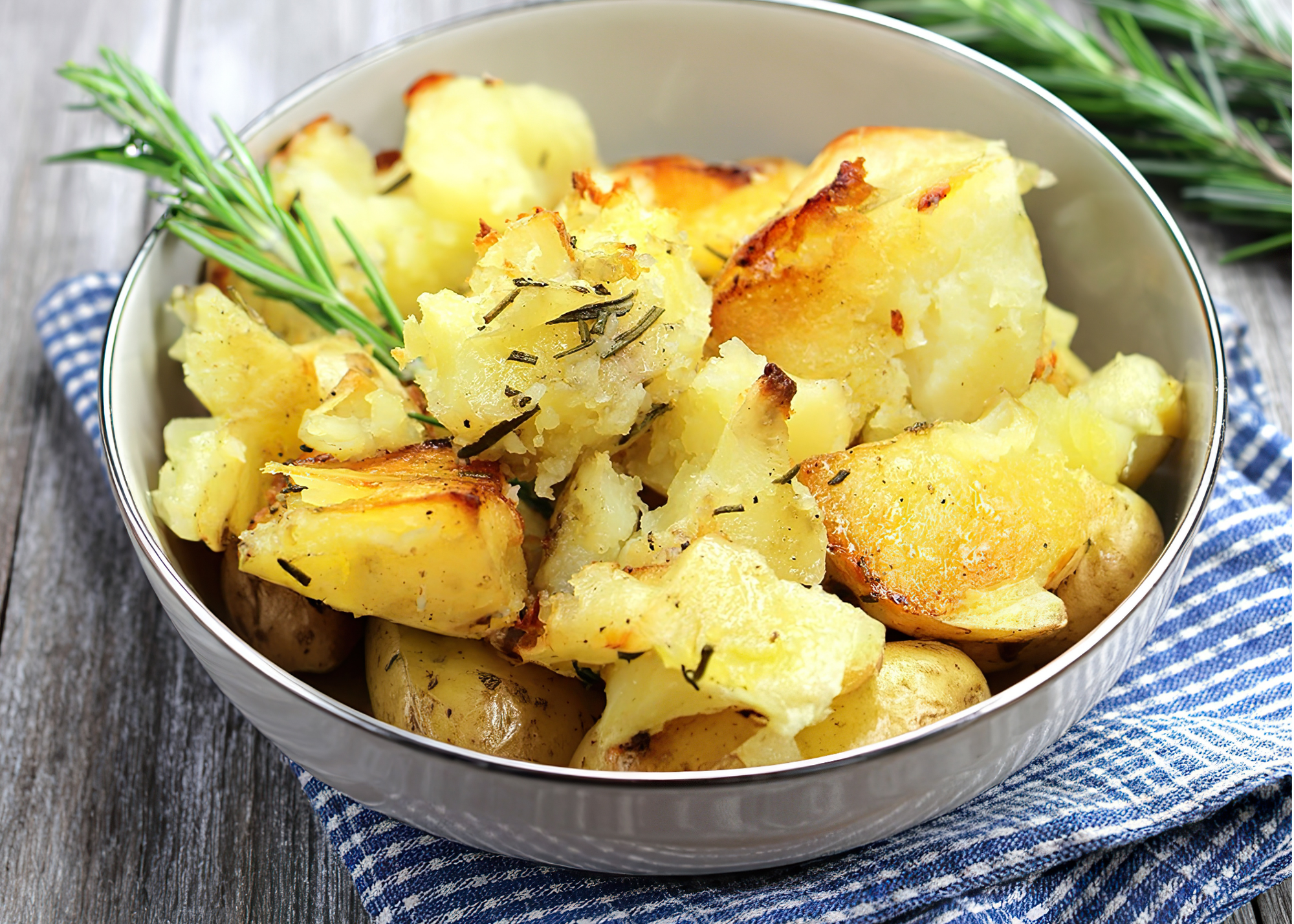 Roasted potatoes in a bowl with a sprig of rosemary