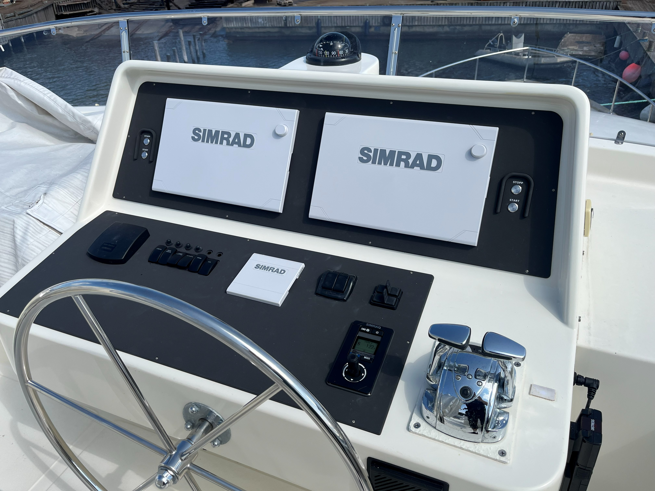Båtens styrekonsoll med to Simrad-navigasjonsskjermer, ratt, autopilot og blanke gasshendler.