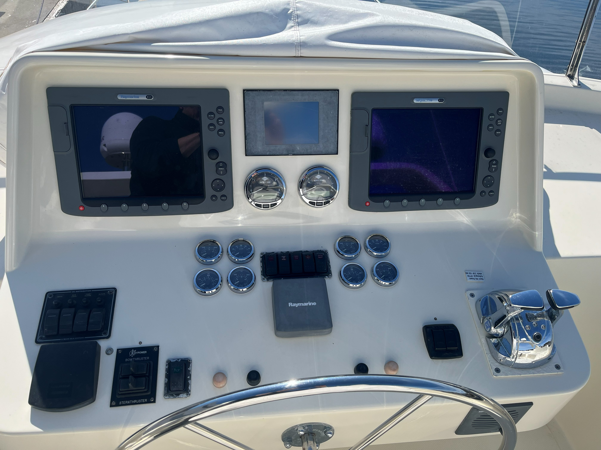 Styrekonsoll på motorbåt med Raymarine-navigasjonsskjermer, motorinstrumenter, bryterpanel, ratt og doble gasshendler.