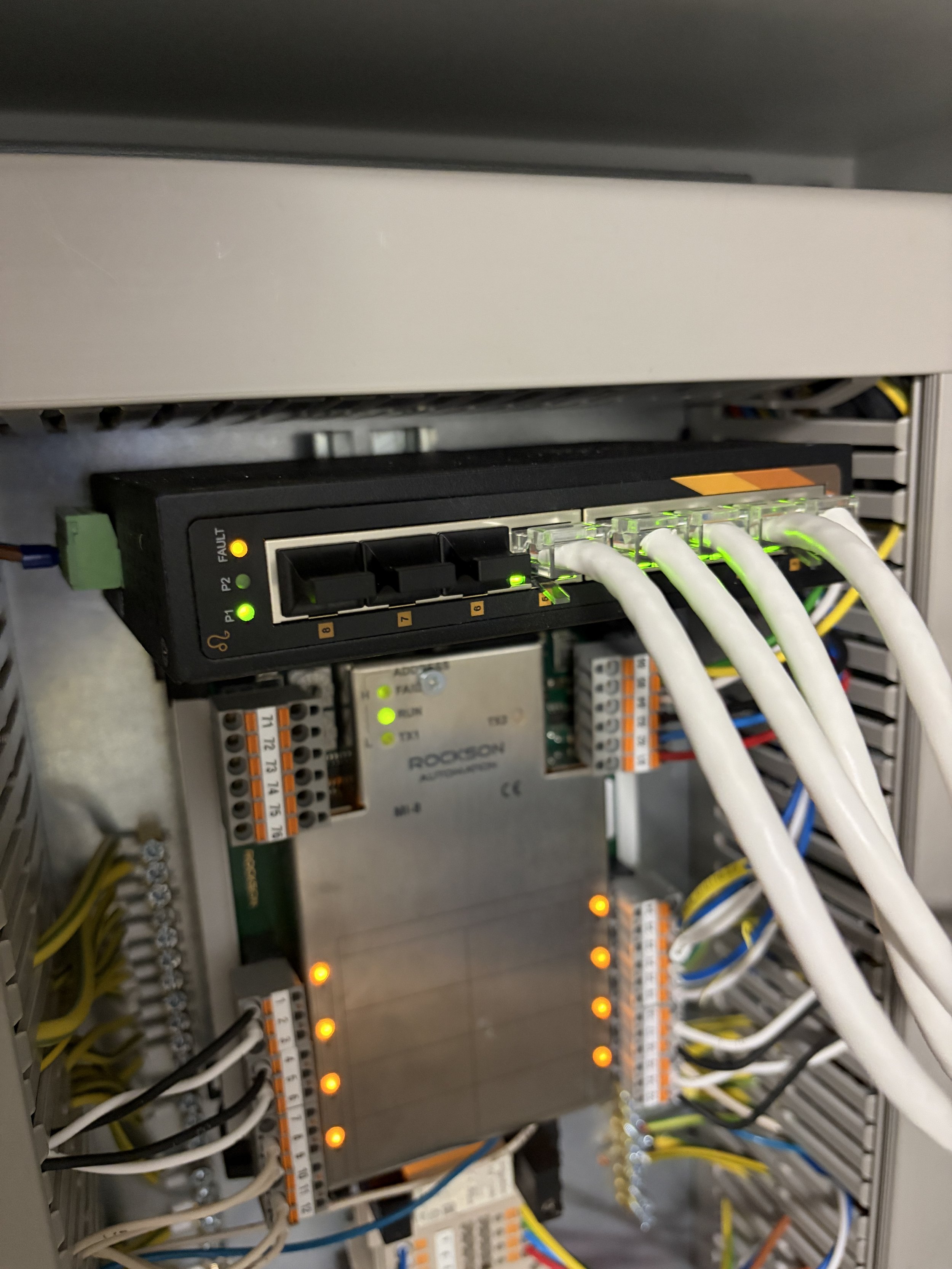 Elektrisk koblingsskap med ledninger og komponenter, noen lamper lyser grønt og oransje.