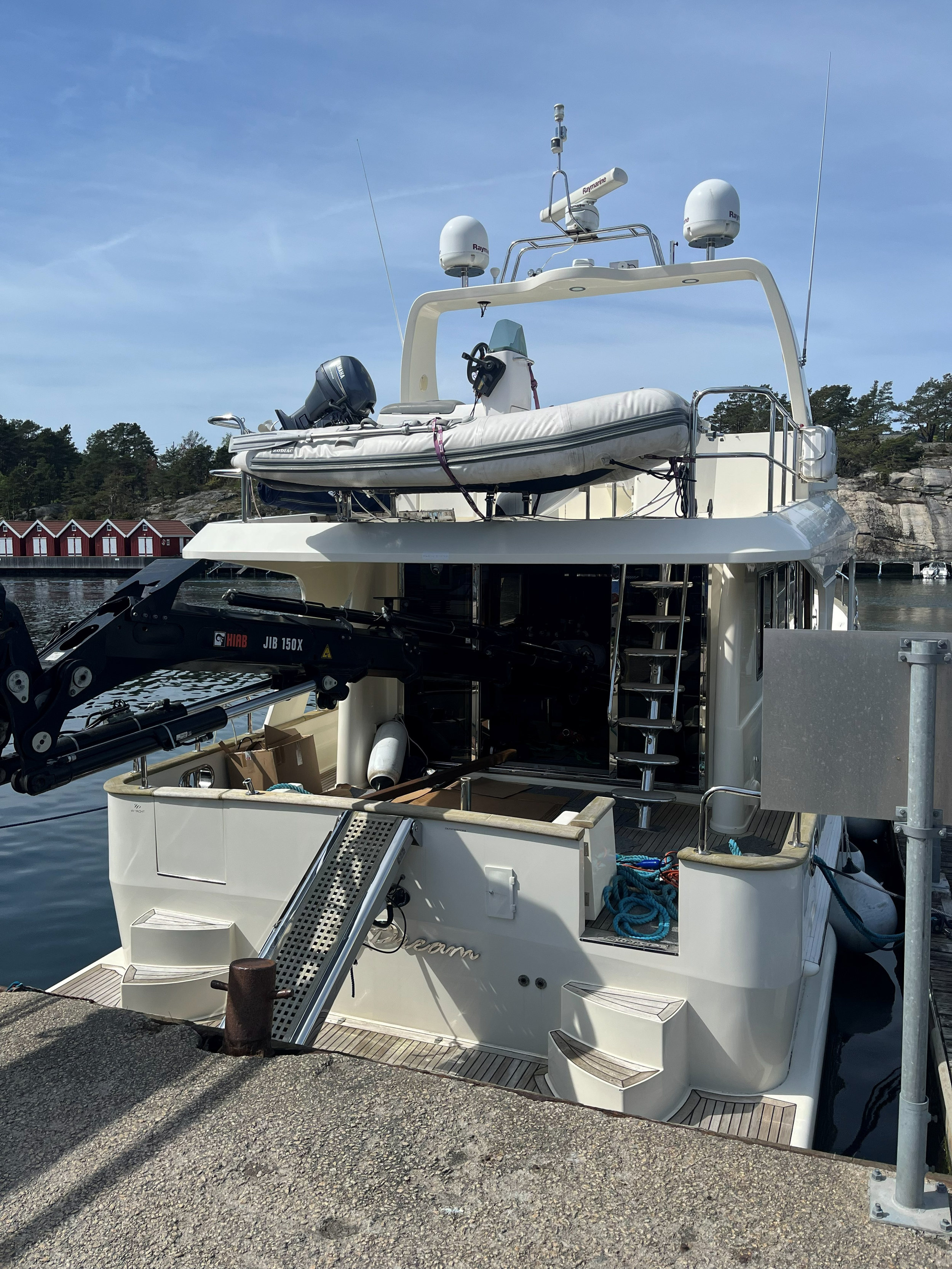 Hvit luksusyacht med jolle, radarantenner og påhengsmotor fortøyd ved brygge i en norsk skjærgård