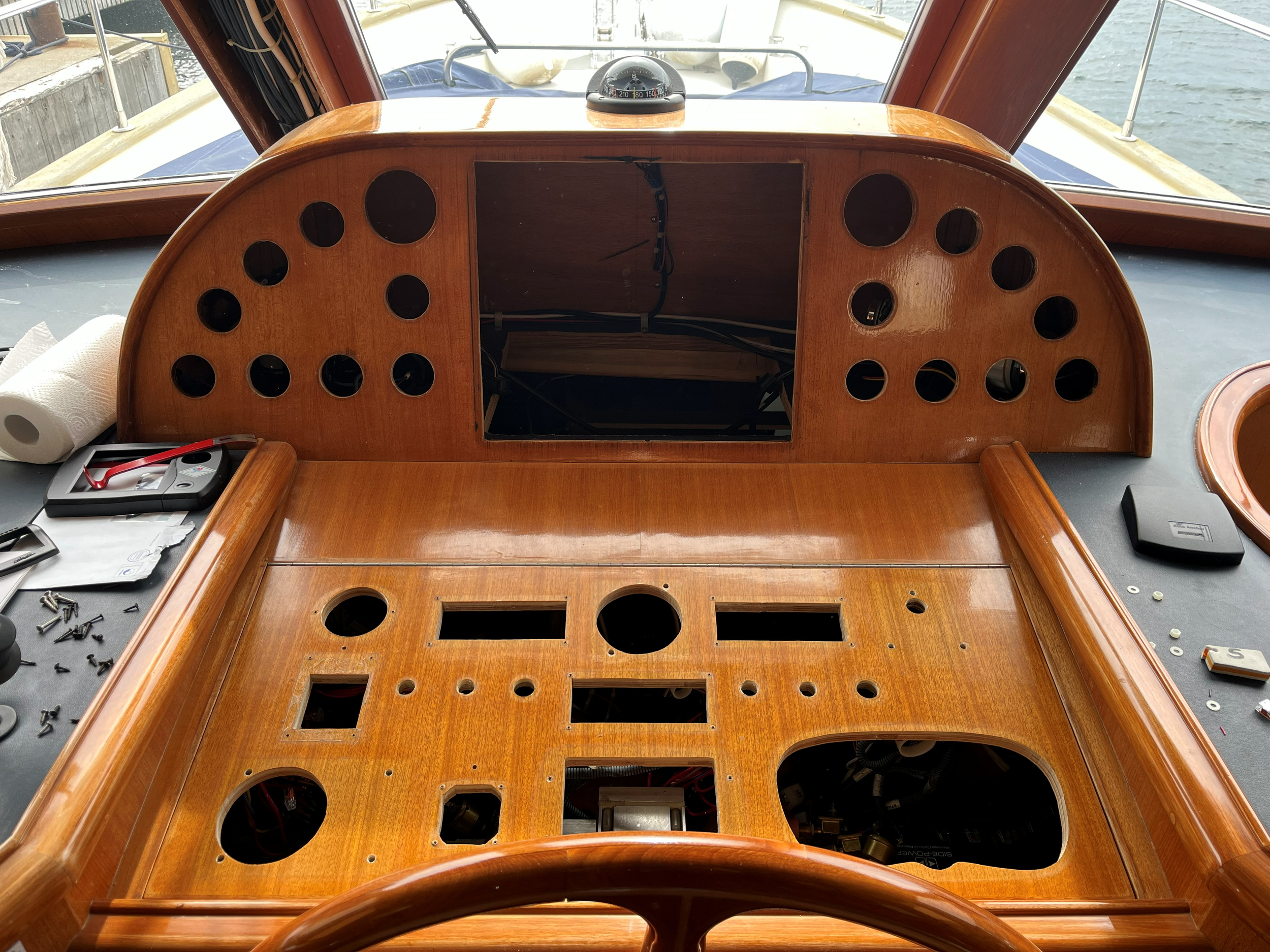 Trepanel i styrehuset på en båt med åpninger for nautiske instrumenter, synlige kabler og kompass.