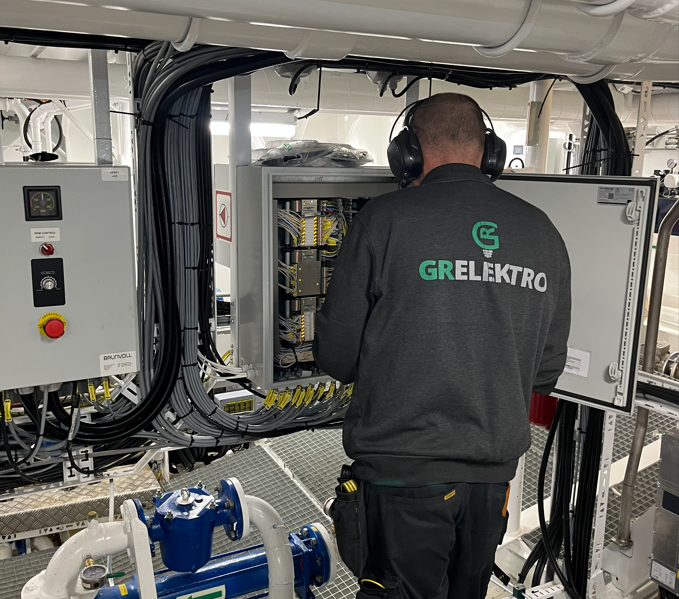 Elektriker fra GR Elektro arbeider i et åpent elektrisk kontrollskap om bord.